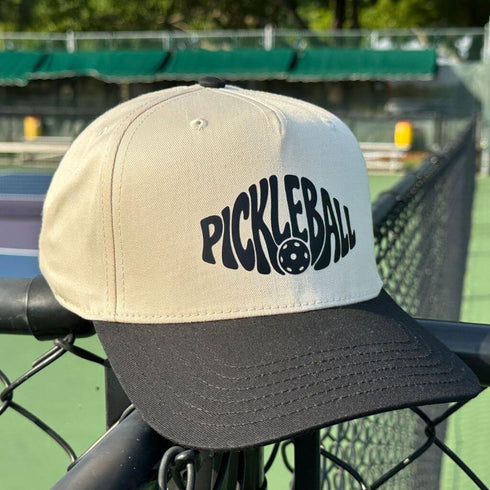 Pickleball cap with black text on a tennis court background